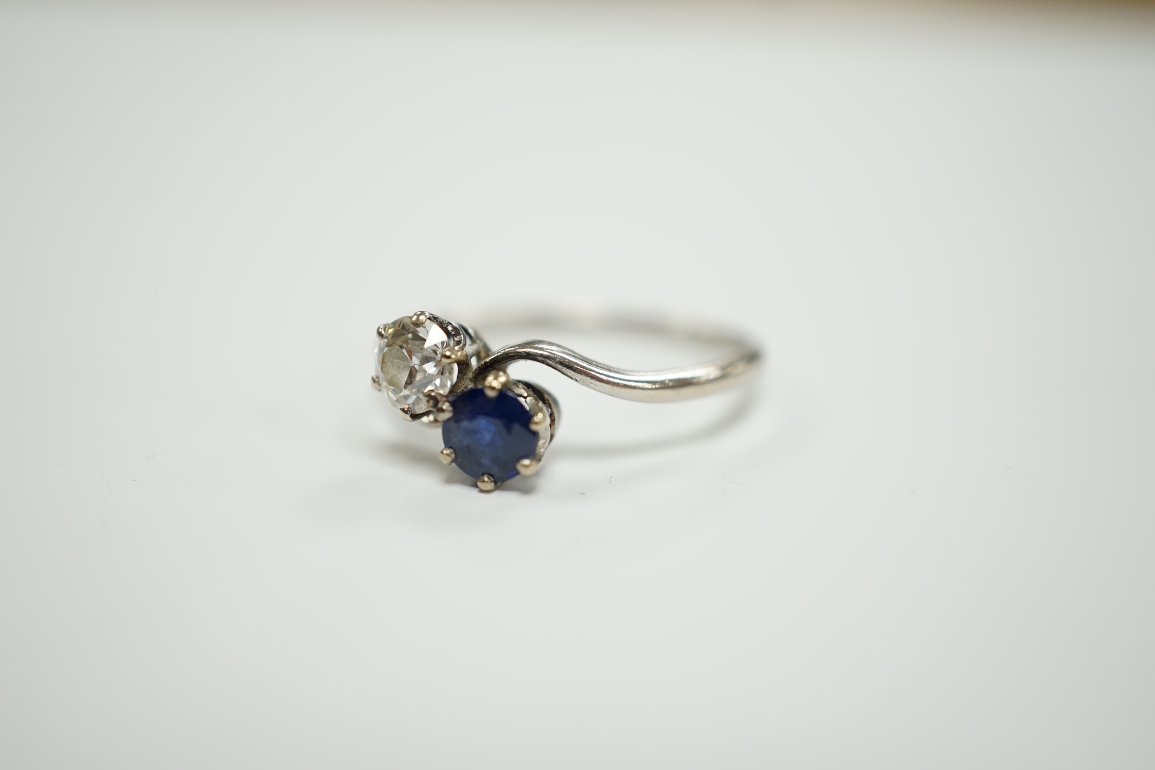A mid 20th century white metal (stamped plat), sapphire and diamond set two stone crossover ring, size Q, gross weight 3.2 grams.